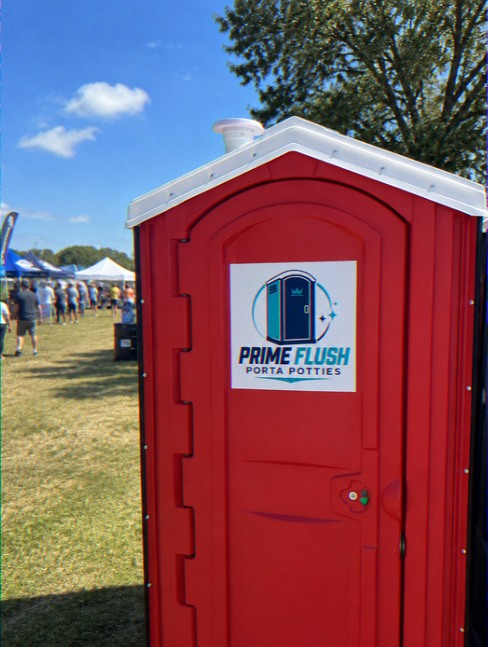 Red portable toilet set up beside marquees at an outdoor event