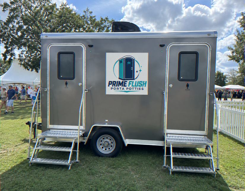 Two-door luxury restroom trailer with steps parked on grass at an event