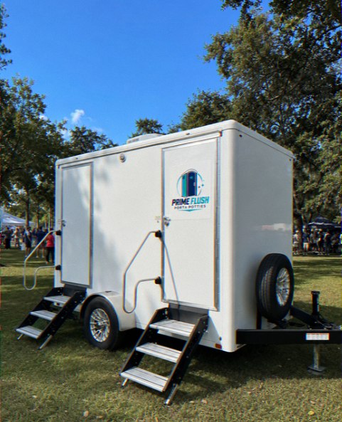 White two-stall restroom trailer with steps set up under trees
